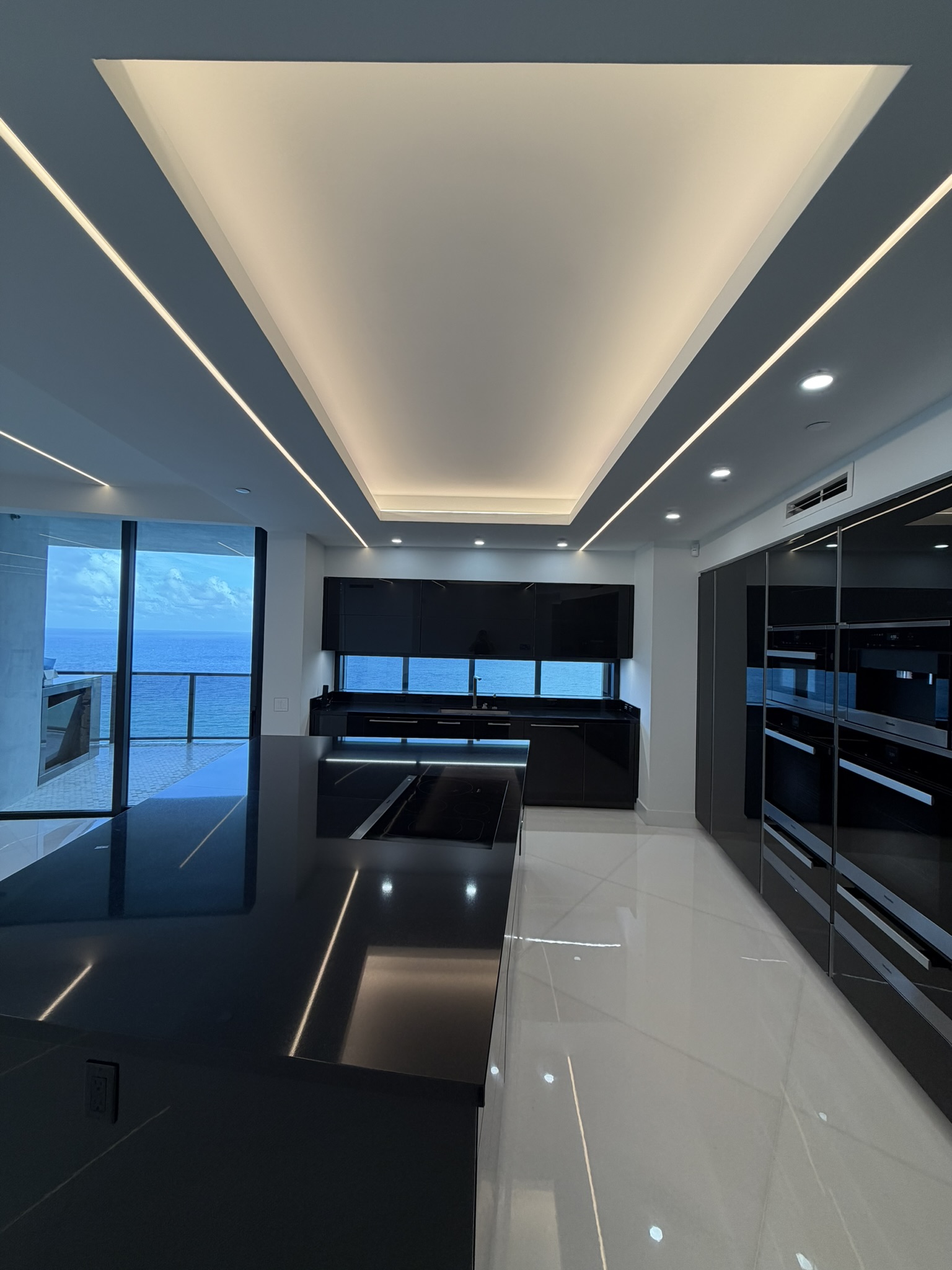 Architectural ceiling lighting above a marble kitchen and island in Sunny Isles